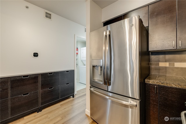 kitchen featuring dark brown cabinets, stainless steel fridge, light hardwood / wood-style floors, and dark stone counters