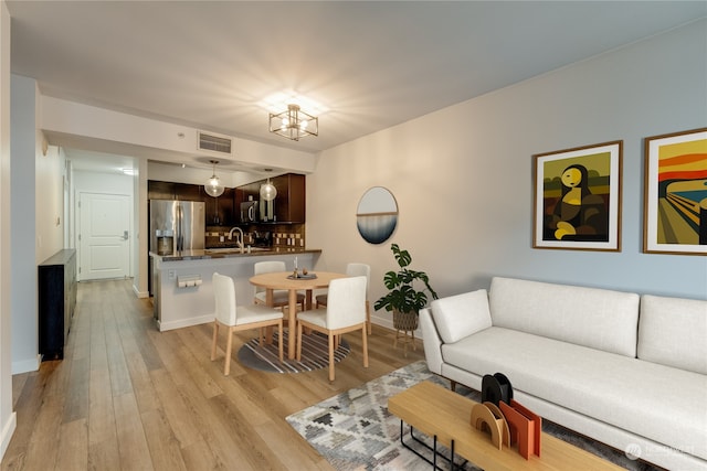 living room with sink, light hardwood / wood-style floors, and an inviting chandelier