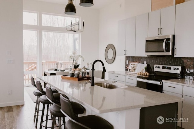 kitchen featuring tasteful backsplash, stainless steel appliances, a kitchen island with sink, sink, and hanging light fixtures