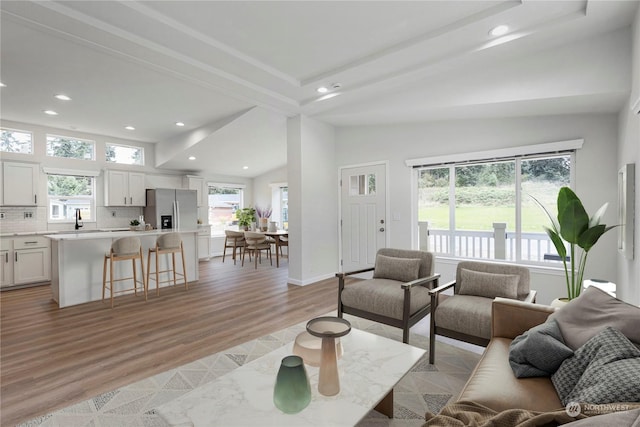 living room featuring light wood-type flooring, lofted ceiling, and sink