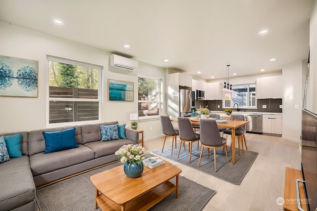 living room with a wall mounted AC, light hardwood / wood-style flooring, and sink