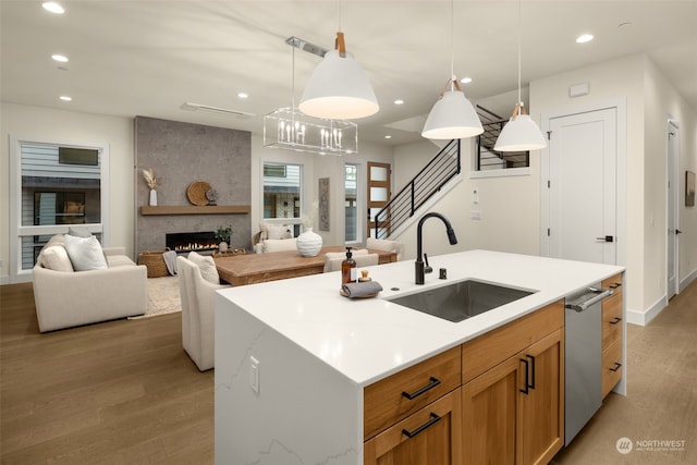 kitchen with stainless steel dishwasher, a large fireplace, a kitchen island with sink, sink, and hanging light fixtures