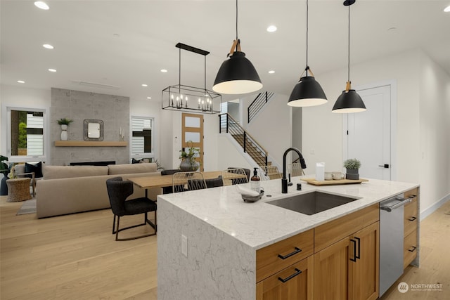 kitchen with a center island with sink, sink, a fireplace, decorative light fixtures, and light stone counters