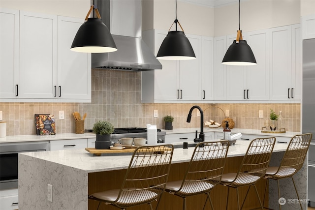 kitchen with a center island with sink, white cabinets, and wall chimney range hood