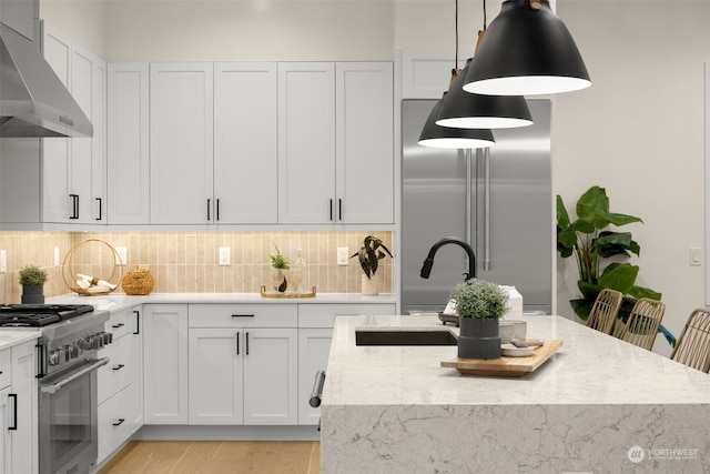 kitchen featuring extractor fan, sink, high quality appliances, white cabinetry, and hanging light fixtures