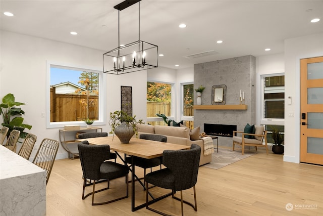 dining room featuring light wood-type flooring, an inviting chandelier, and a tiled fireplace