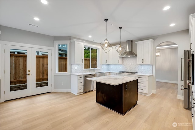 kitchen featuring a center island, wall chimney range hood, hanging light fixtures, light hardwood / wood-style floors, and stainless steel appliances