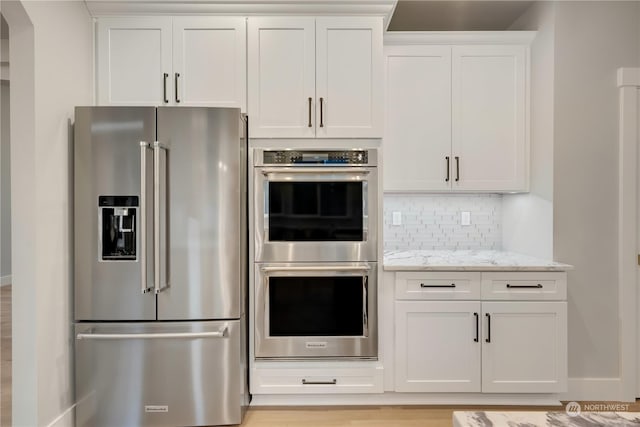 kitchen featuring light stone countertops, appliances with stainless steel finishes, white cabinets, and decorative backsplash