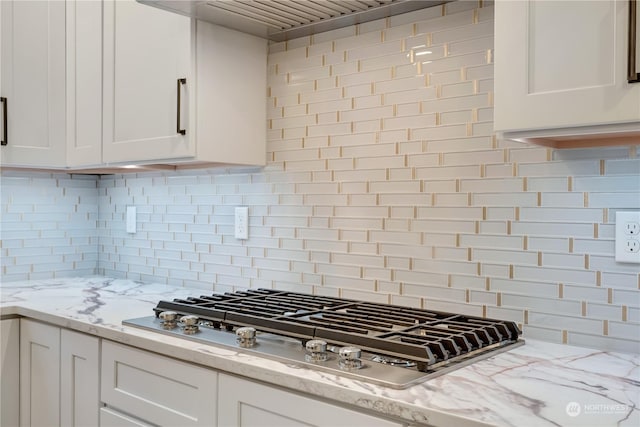 kitchen with decorative backsplash, white cabinets, light stone counters, and stainless steel gas cooktop