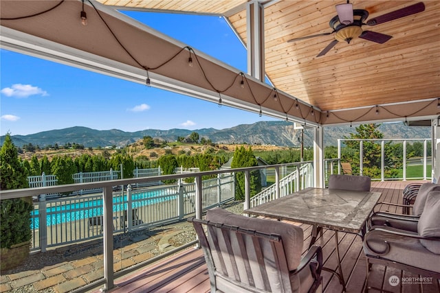 wooden terrace with a mountain view, a fenced in pool, and ceiling fan