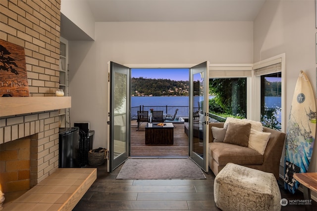 living room with a water view, a brick fireplace, and dark wood-type flooring