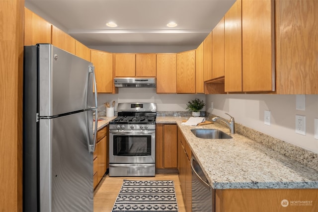 kitchen with appliances with stainless steel finishes, light hardwood / wood-style flooring, light stone counters, and sink