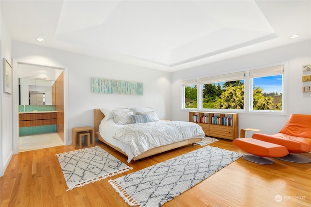 bedroom with a raised ceiling, ensuite bath, and light wood-type flooring