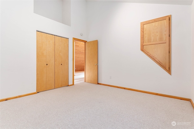 unfurnished bedroom with light carpet, a high ceiling, and a closet