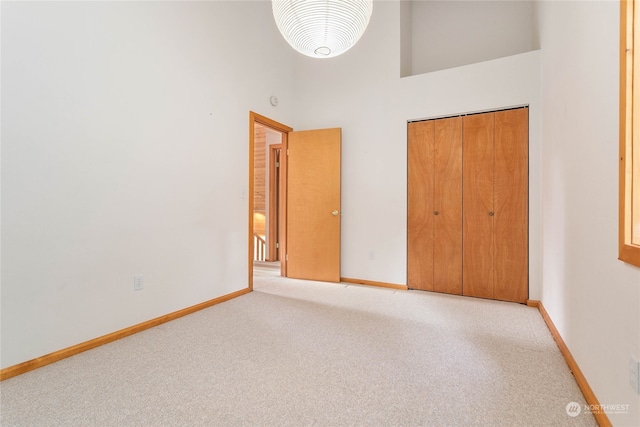 unfurnished bedroom featuring light carpet, a high ceiling, and a closet