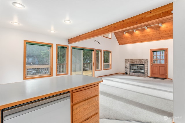 kitchen with light brown cabinets, rail lighting, a brick fireplace, vaulted ceiling with beams, and carpet floors