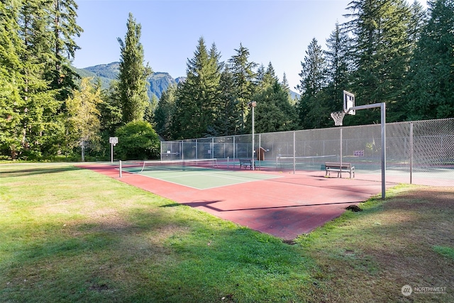 view of sport court with basketball hoop, a mountain view, and a yard