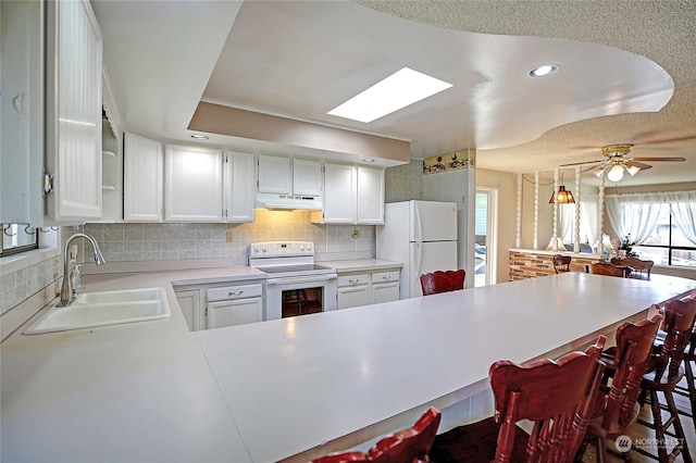 kitchen with kitchen peninsula, white appliances, white cabinetry, and sink