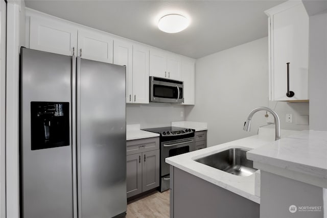 kitchen with gray cabinetry, white cabinetry, sink, stainless steel appliances, and light stone counters