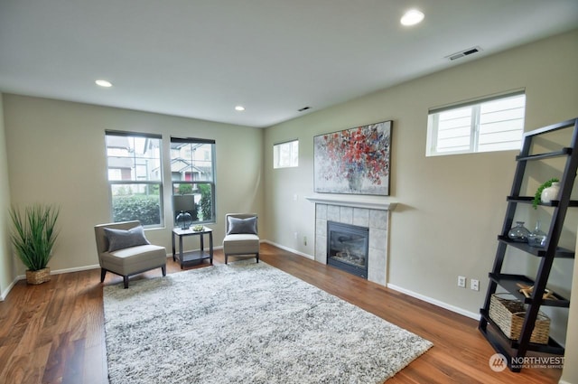 sitting room with a tile fireplace, plenty of natural light, and dark wood-type flooring