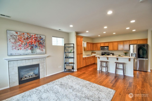 kitchen featuring appliances with stainless steel finishes, dark hardwood / wood-style floors, a kitchen breakfast bar, a tiled fireplace, and a kitchen island with sink