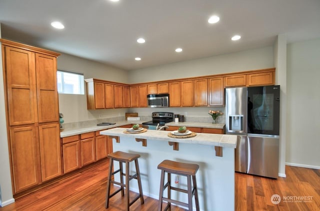 kitchen featuring dark hardwood / wood-style flooring, a breakfast bar, a center island, and appliances with stainless steel finishes