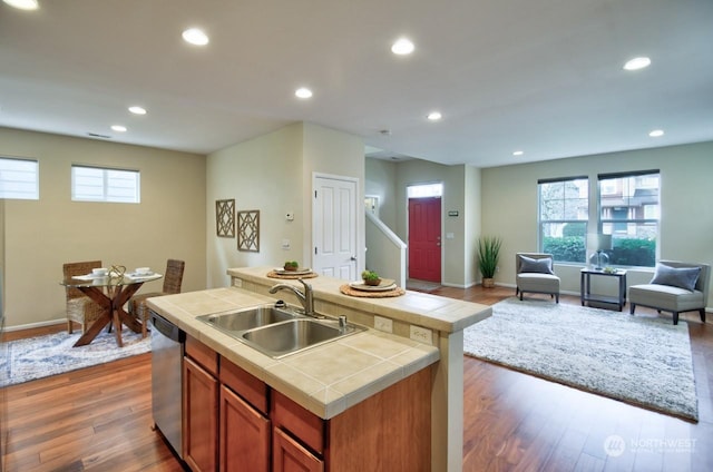 kitchen featuring sink, tile countertops, a center island with sink, dark hardwood / wood-style flooring, and dishwasher