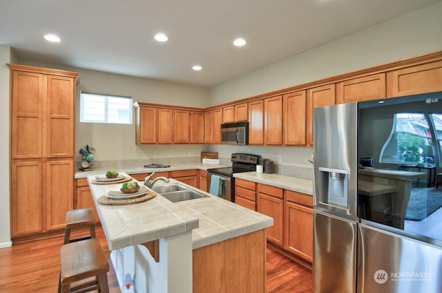 kitchen featuring sink, a center island with sink, appliances with stainless steel finishes, tile counters, and hardwood / wood-style floors