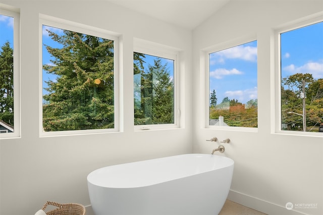 bathroom with tile patterned floors, lofted ceiling, a bath, and a wealth of natural light