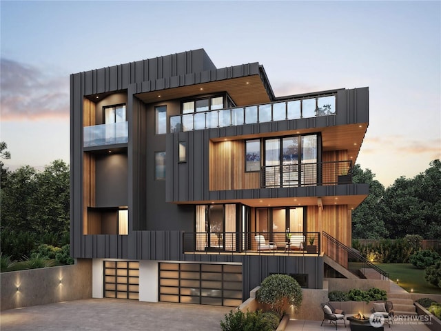 back of property featuring board and batten siding, a balcony, a garage, driveway, and stairs