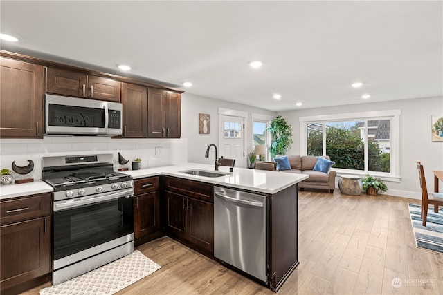 kitchen with sink, appliances with stainless steel finishes, tasteful backsplash, light hardwood / wood-style floors, and kitchen peninsula