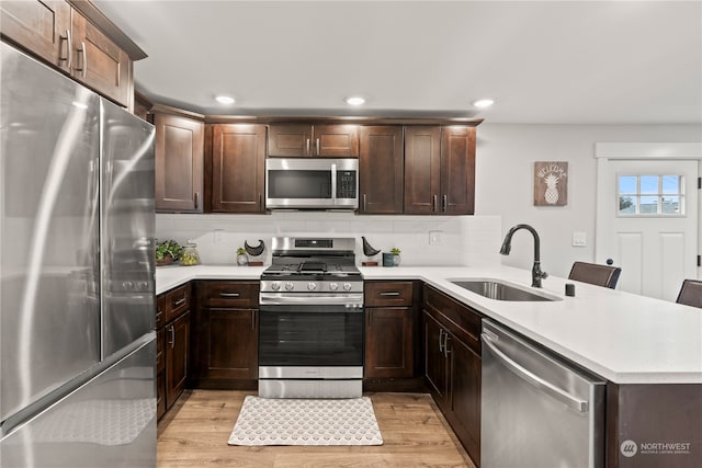 kitchen featuring kitchen peninsula, a breakfast bar, stainless steel appliances, sink, and light hardwood / wood-style floors