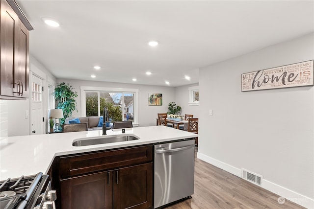 kitchen with kitchen peninsula, appliances with stainless steel finishes, light wood-type flooring, dark brown cabinets, and sink