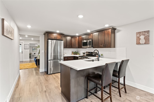 kitchen featuring sink, light hardwood / wood-style flooring, appliances with stainless steel finishes, dark brown cabinets, and kitchen peninsula