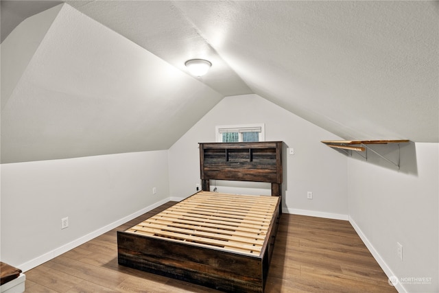 bedroom featuring lofted ceiling, wood-type flooring, and a textured ceiling