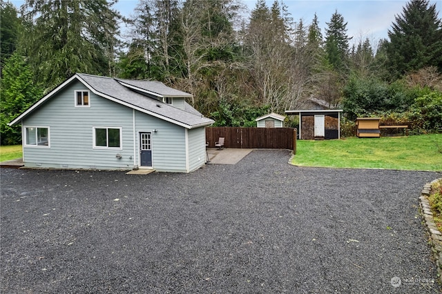 rear view of property featuring a lawn, a storage unit, and a patio