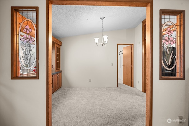 carpeted spare room featuring a textured ceiling, vaulted ceiling, and a notable chandelier