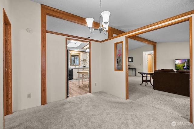 interior space with vaulted ceiling with skylight, a notable chandelier, light colored carpet, and a textured ceiling