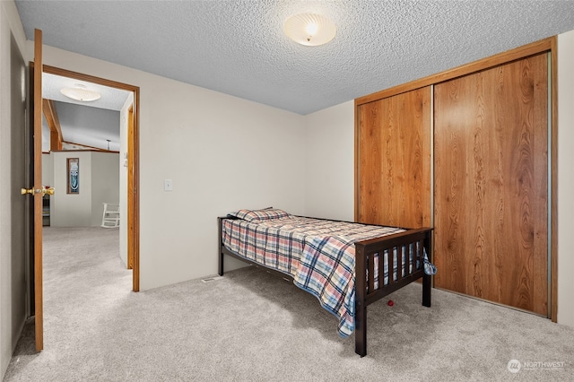 bedroom with a textured ceiling, light colored carpet, vaulted ceiling, and a closet