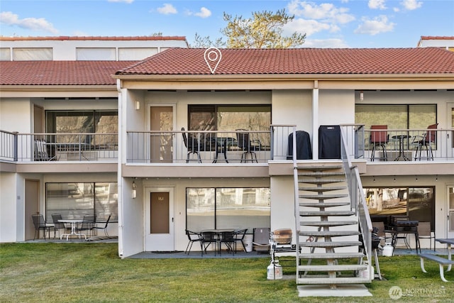 back of property with a tile roof, stairs, a lawn, stucco siding, and a patio area