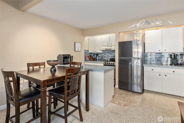 kitchen with appliances with stainless steel finishes, white cabinetry, under cabinet range hood, and decorative backsplash