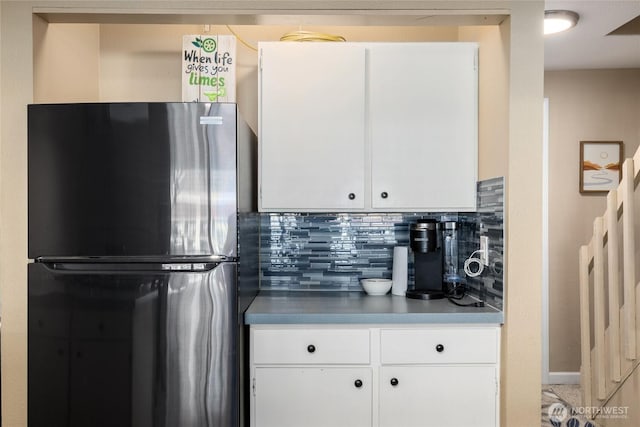 kitchen featuring freestanding refrigerator, white cabinetry, and decorative backsplash