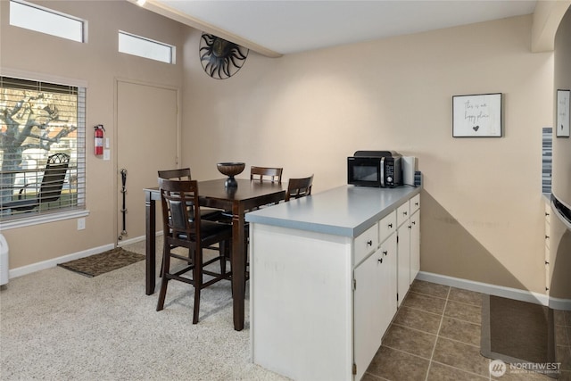 kitchen with light countertops, white cabinets, black microwave, a peninsula, and baseboards