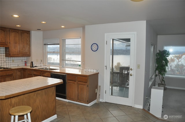 kitchen with tile countertops, sink, tile patterned flooring, black dishwasher, and kitchen peninsula