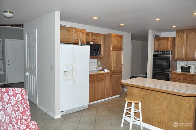 kitchen featuring tasteful backsplash, black appliances, light tile patterned floors, tile countertops, and a breakfast bar area