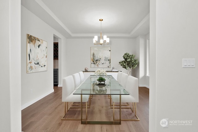 dining space featuring an inviting chandelier, wood-type flooring, and a raised ceiling