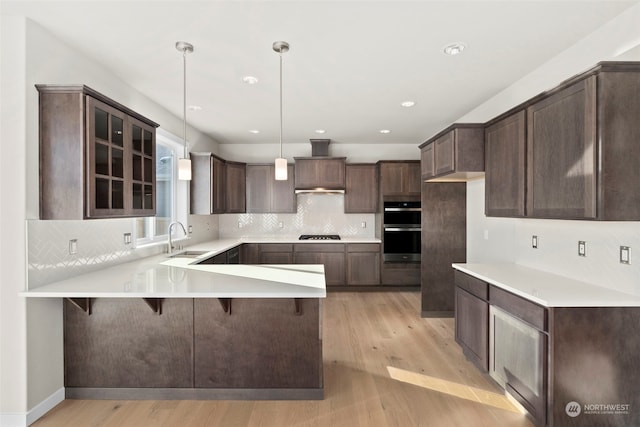 kitchen featuring sink, double oven, decorative light fixtures, kitchen peninsula, and light wood-type flooring