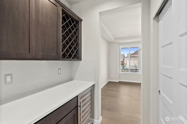 bar featuring wine cooler, light hardwood / wood-style flooring, dark brown cabinets, and backsplash