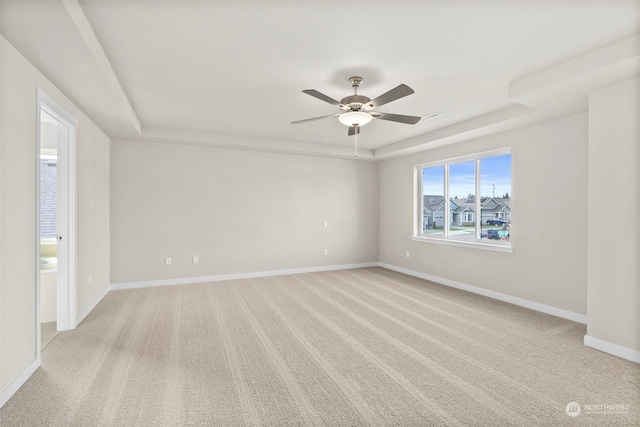 carpeted empty room featuring ceiling fan and a raised ceiling