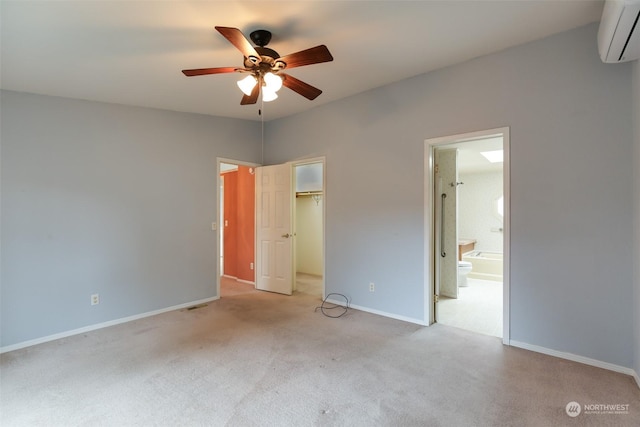 unfurnished bedroom with ensuite bath, a spacious closet, light carpet, a wall unit AC, and a closet